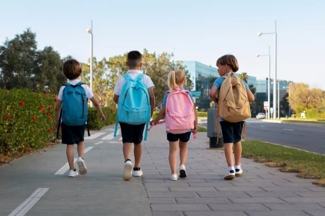 Cuatro niños caminando de espaldas por la calle saliendo de la escuela