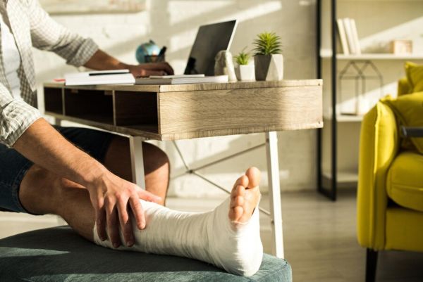 Hombre con pierna lesionada en su hogar mientras revisa su computadora
